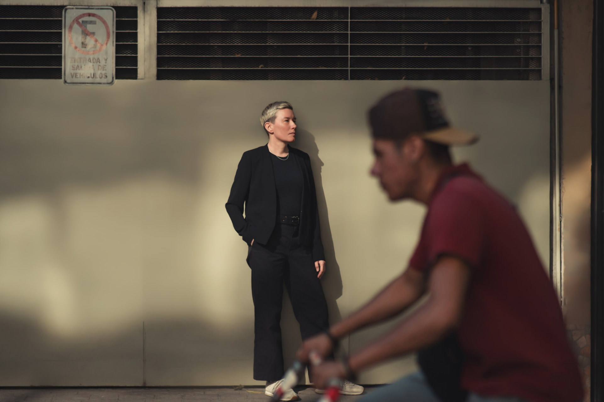 Retrato de pie junto a una pared en la calle, con un ciclista en primer plano