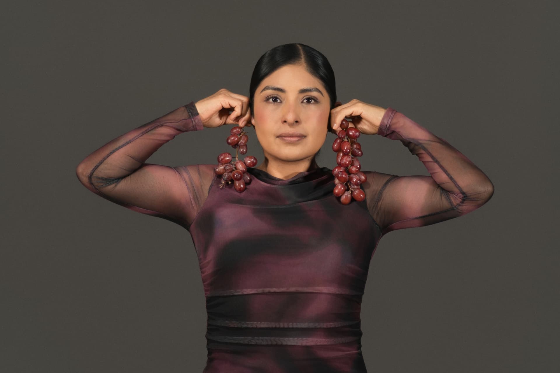 Retrato en estudio con racimos de uvas sostenidos como aretes